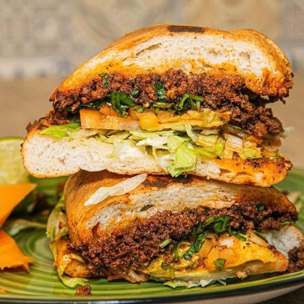 A large, sliced Mexican torta sandwich with meat, lettuce, and cheese on a green plate.