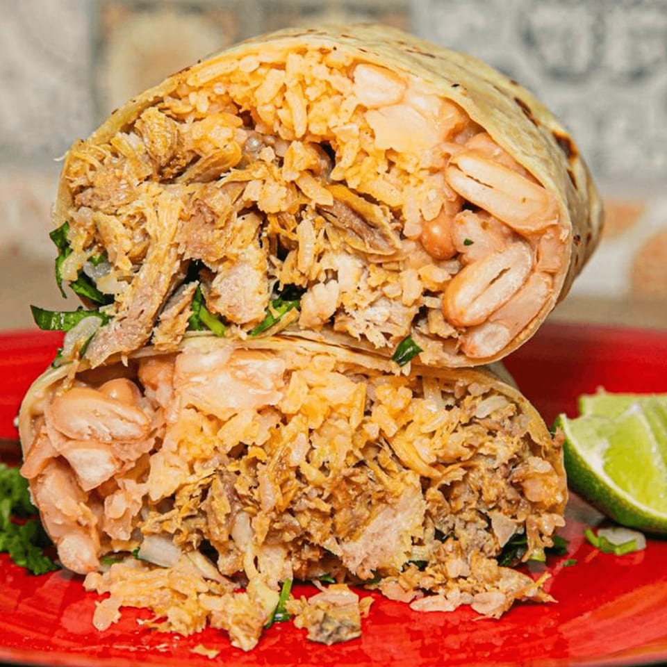 A large, cut burrito filled with rice, beans, and shredded meat, served on a red plate with lime.