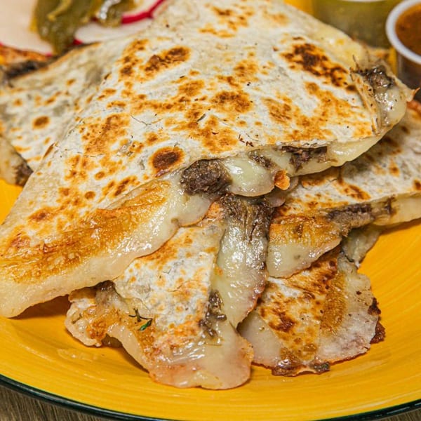 Close-up of golden-brown quesadillas filled with melted cheese and meat, served on a yellow plate.