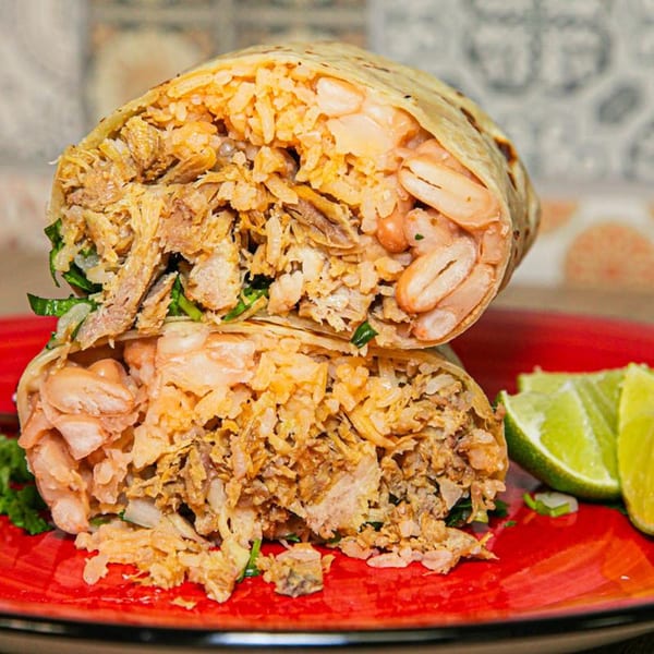A large, cut burrito filled with rice, beans, and shredded meat, served with lime wedges.