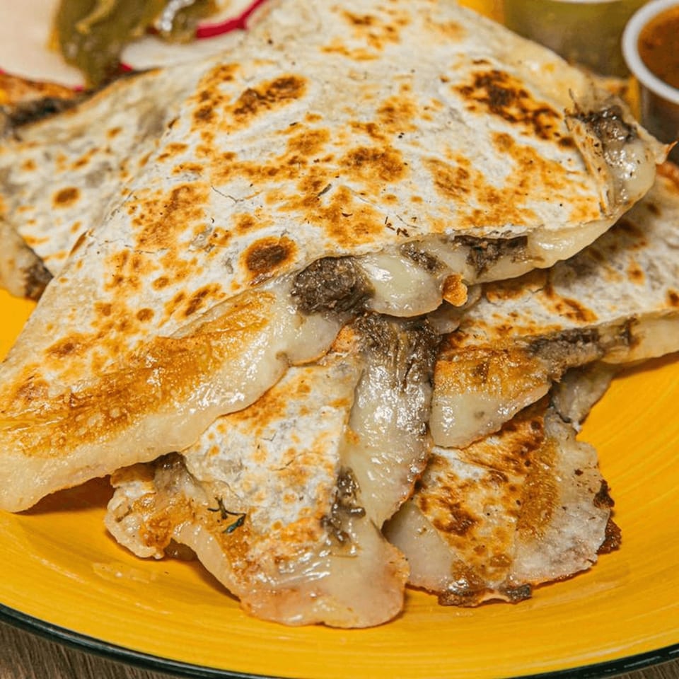 Close-up of golden-brown quesadillas with melted cheese and meat filling on a yellow plate.